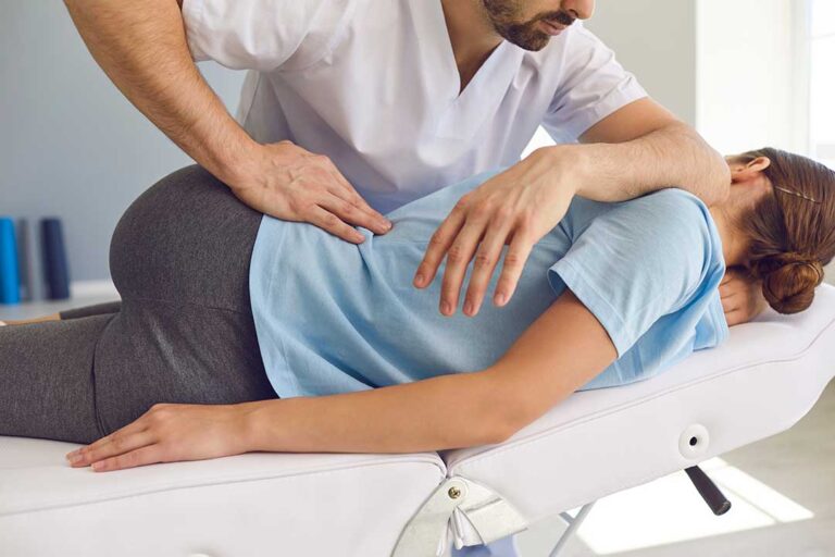 A person applying an ice pack to their lower back while seated in a comfortable living room chair.